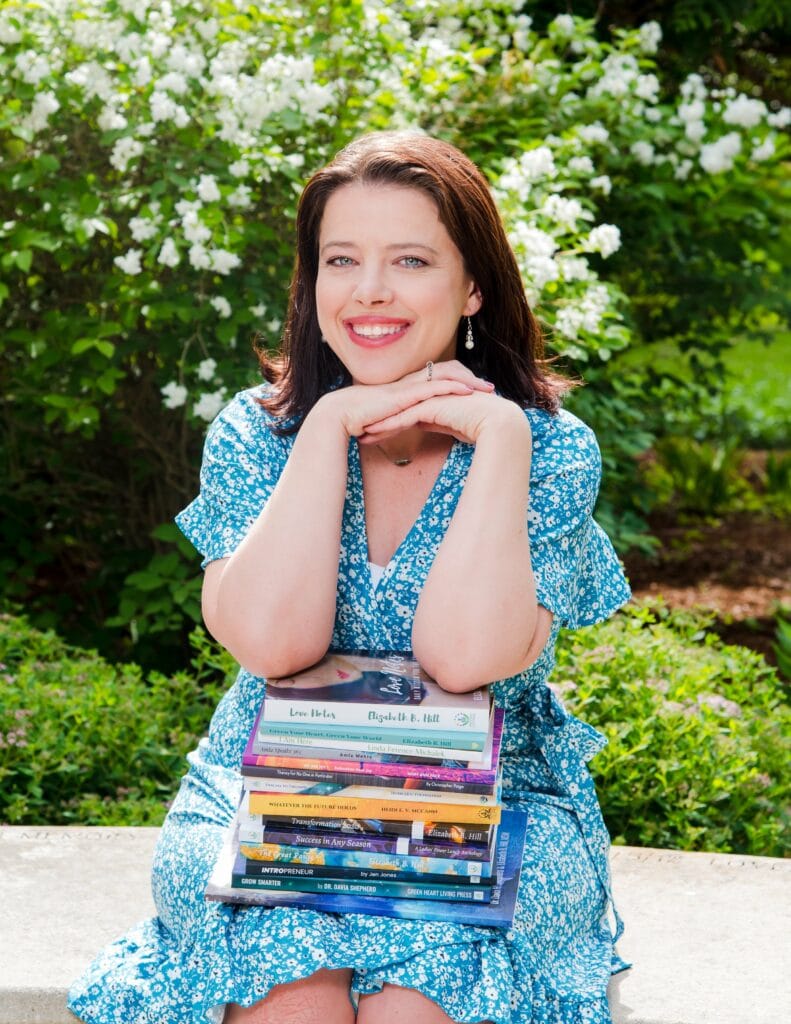 Colleen Brunetti smiling posing outside with a stack of books on her lap