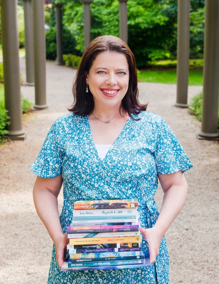 Colleen Bruneti smiling posing outside with a stack of books in her hands